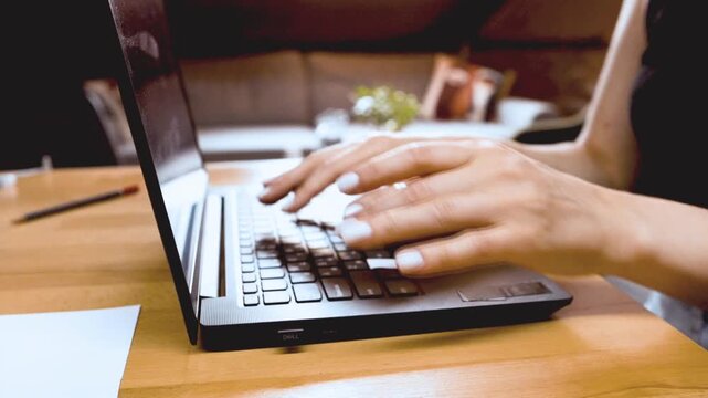 Female hands typing on laptop keyboard close up at wooden desk. Concept of office work, business communication, digital productivity, and modern workplace.