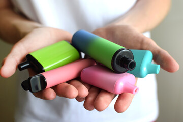 Many colorful electronic cigarettes in the hands of a teenager. Vaping with nicotine. Danger for teenagers. © Oksana