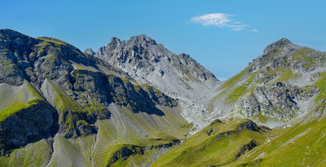 Majestic mountain landscape featuring rugged peaks and lush green valleys under a clear blue sky,...