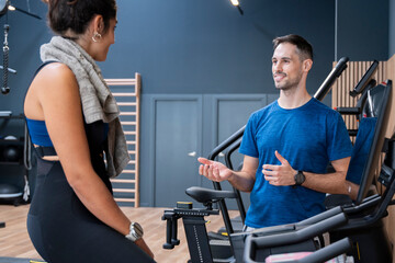 Personal trainer talking with female client during workout session at a modern gym