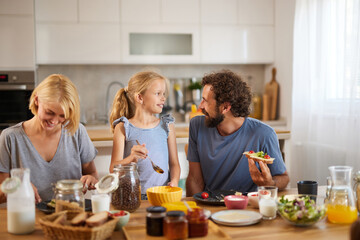 A cheerful family shares a morning meal in their cozy kitchen. Everyone participates, enjoying food and lighthearted conversation, creating a joyful atmosphere.