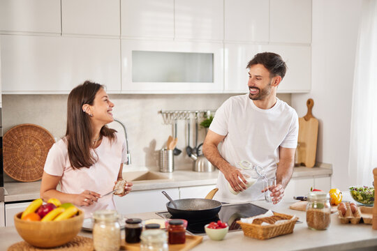In a modern kitchen, a couple shares joyful moments while preparing a meal. Fresh fruits, vegetables, and various ingredients are spread out, enhancing their cooking experience. - Powered by Adobe
