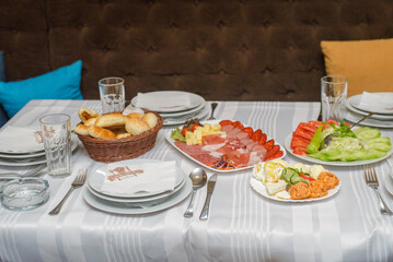 A table with three dishes. Cream, fun and paprika in sour cream on one plate. Finely chopped sausages and bacon on another plate. Cucumber, tomato, cabbage and onion as a salad on the third plate and 