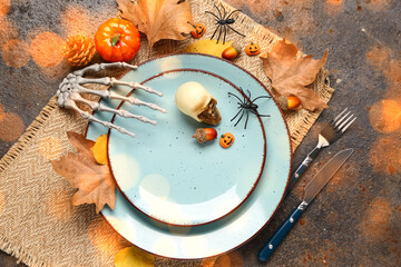 Halloween table setting with skeleton hand and autumn decorations on dark grunge background