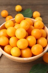 Ripe yellow cherry plums and leaves on wooden table, closeup