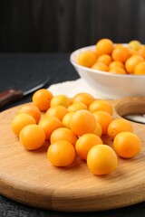 Ripe yellow cherry plums, wooden board and knife on black table, closeup
