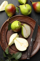 Fresh ripe pears, knife and green leaves on black table, flat lay