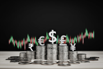 Stack of coins in rows with symbols of international currencies, yen, euro, dollar, pound, rupee and trading chart. Concept of finance, currency exchange rates and stock market investment.