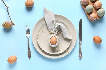 Beautiful table setting with Easter eggs and tree branch on blue background