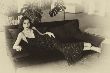 sepia color black and white photo 20s old style retro lady roaring sexy woman fashion model posing with long legs. Flapper girl lying on sofa. holiday make-up face lips hair long dress gloves 1920s