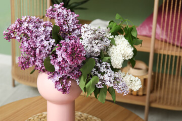 Vase with lilacs branches on coffee table in stylish living room, closeup