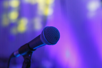A microphone stands ready for use under colorful stage lights, highlighting its fine mesh detail and sleek design.