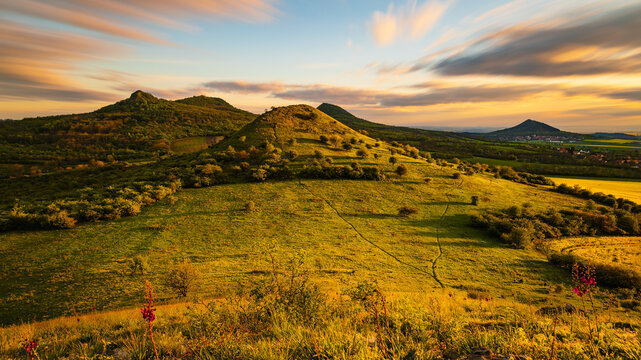 Sunset over the rolling hills of the Bohemian Central Highlands in the Czech Republic, with vibrant yellow fields and dramatic skies creating a stunning landscape view.