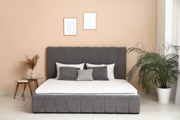 New orthopedic mattress on stylish bed near beige wall in room