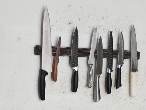 Well-used Kitchen Knives on Magnetic Holder Against Grungy White Wall, Reflecting Culinary History and Everyday Utility