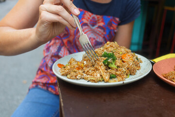 A person savors a plate of thai street food, spicy fried rice with vegetables.