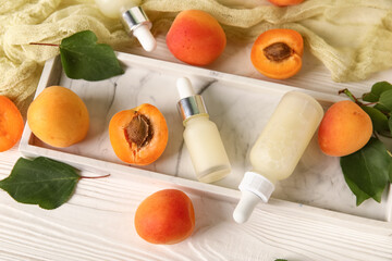 Bottles of cosmetic oil with fresh apricots on white wooden background