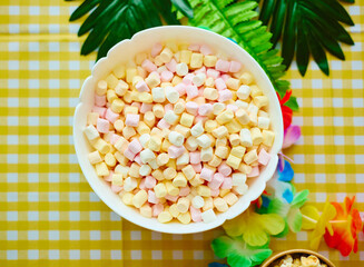Top view of a white bowl filled with colorful mini marshmallows on a yellow checkered tablecloth