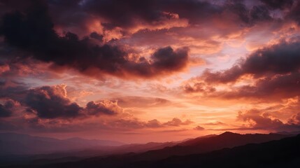 Fototapeta premium Vibrant sunset sky casting warm orange and red light over a tranquil mountain landscape with dramatic colorful clouds