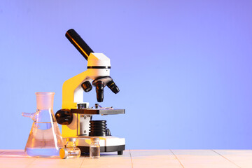 Modern microscope with laboratory flask and ampules on white tile table