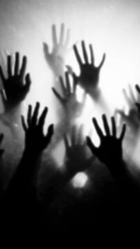 Dark, blurred silhouette of human hands and zombie palms on a white, foggy background in slow motion. Halloween concept