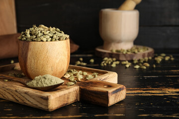 Bowl of cardamom spice and spoon with powder on black wooden background