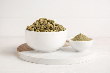 Bowls with cardamom spice and powder on white wooden background