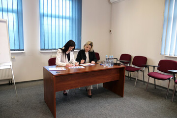 Two women working together in a modern office: signing documents and discussing charts on a flipchart during a work meeting