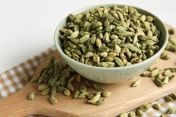 Bowl and wooden board with cardamom spice on white background, closeup