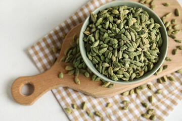 Bowl and wooden board with cardamom spice on white background