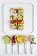 Sushi roll with eel on a white plate on a white background with ingredients on white spoons isolated