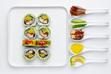 Sushi roll with eel on a white plate on a white background with ingredients on white spoons isolated
