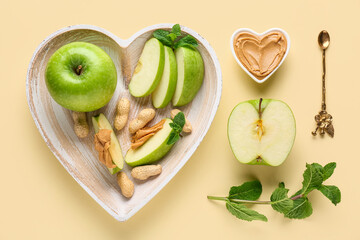 Plate with cut fresh apple, mint and bowl of sweet peanut butter on yellow background