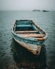 Obraz premium Misty Solitude: An Old Wooden Boat on a Gloomy, Rainy Shoreline
