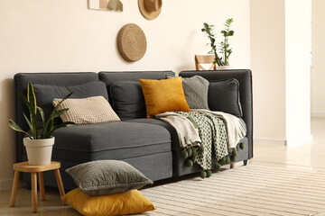 Comfortable dark sofa with soft pillows and houseplants near white wall in living room