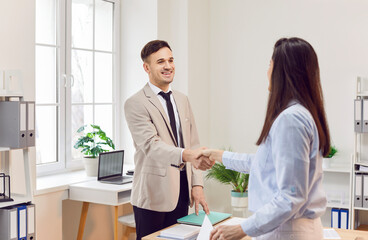 Fototapeta premium Happy businessman shaking hands with a female client or colleague in an office setting. Partnership, teamwork, or agreement and deal, professional interaction between the two individuals.