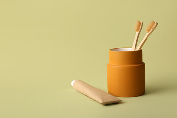 Holder with bamboo toothbrushes and tube of paste on green background