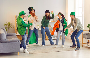Group of happy, cheerful friends dressed up in funny costumes celebrating Saint Patrick's Day, having a party at home, dancing in the living room and having jolly good fun together