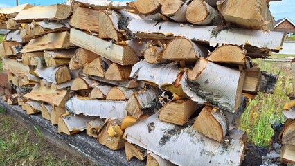 Stack of cut birch firewood logs outdoors on a summer day