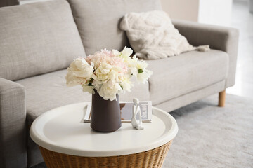 Bouquet of peony flowers on table near sofa in living room