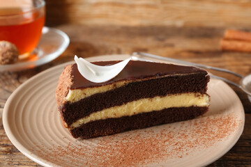 Plate with piece of sweet chocolate cake and glass cup of hot tea on wooden background, closeup
