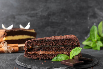 Black board with piece of sweet chocolate cake and mint leaves on dark background