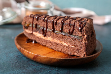 Wooden plate with piece of sweet chocolate cake on blue background