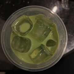 Cold green beverage with ice cube topping. 