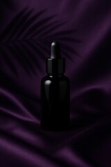 Naklejka premium Black dropper bottle mockup on purple silk fabric background