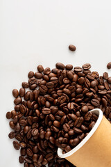 Coffee Beans Spilled from Paper Cup on White Surface