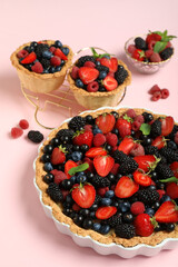 Sweet tart and tartlets with different fresh berries on pink background