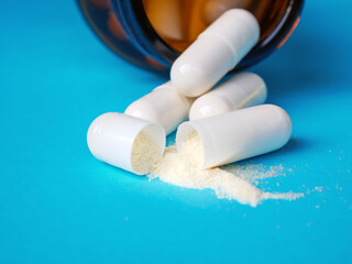White pills, open capsules with powder on blue background, close-up