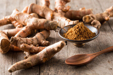 Fresh Turmeric Root with Ground Spice on Wooden Table Background