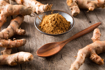 Ground Turmeric Powder in Bowl Surrounded by Fresh Roots on Wood